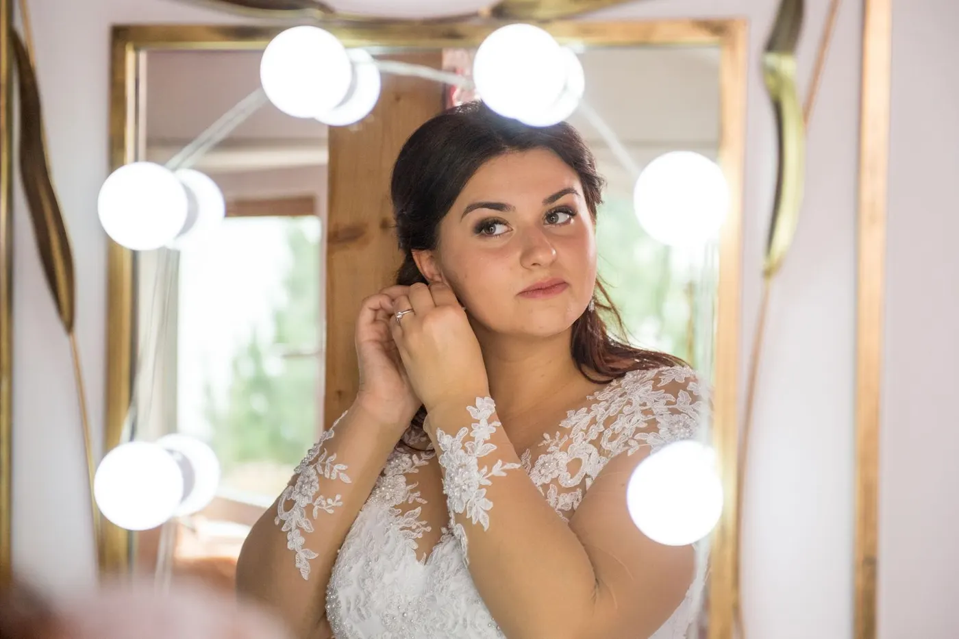 A bride adjusting an earring while looking into a mirror before the ceremony