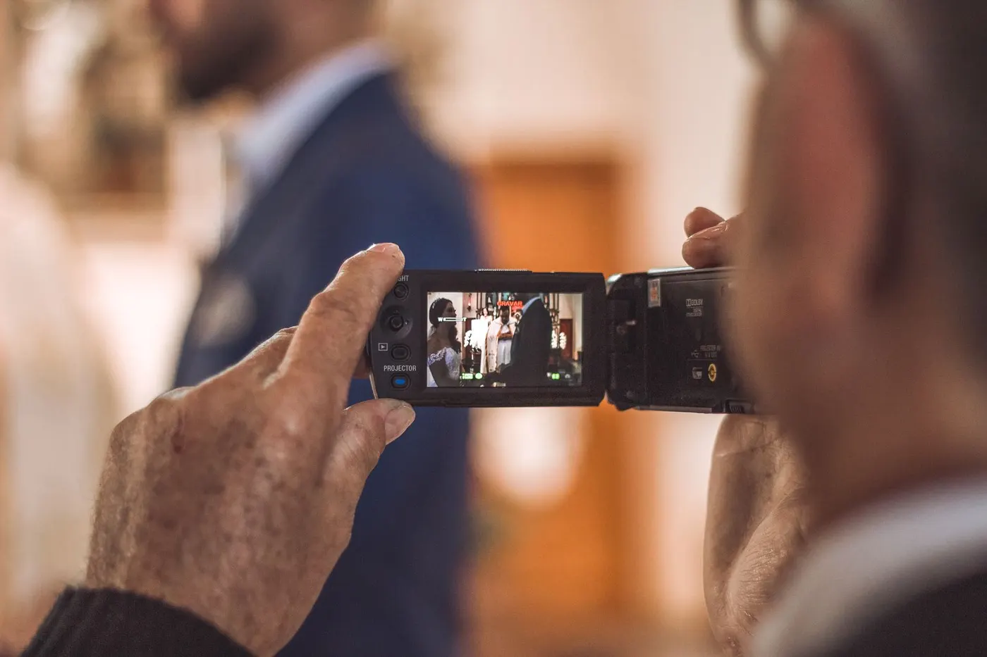 An older guest’s hands filming a wedding with a small camcorder