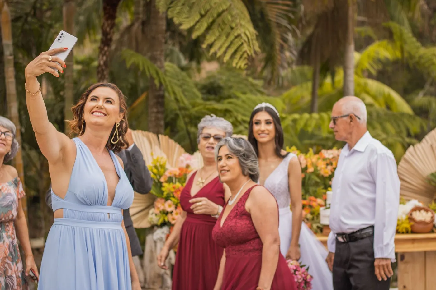 Wedding guests and the bride crowding around a phone for a photo at an outdoor reception