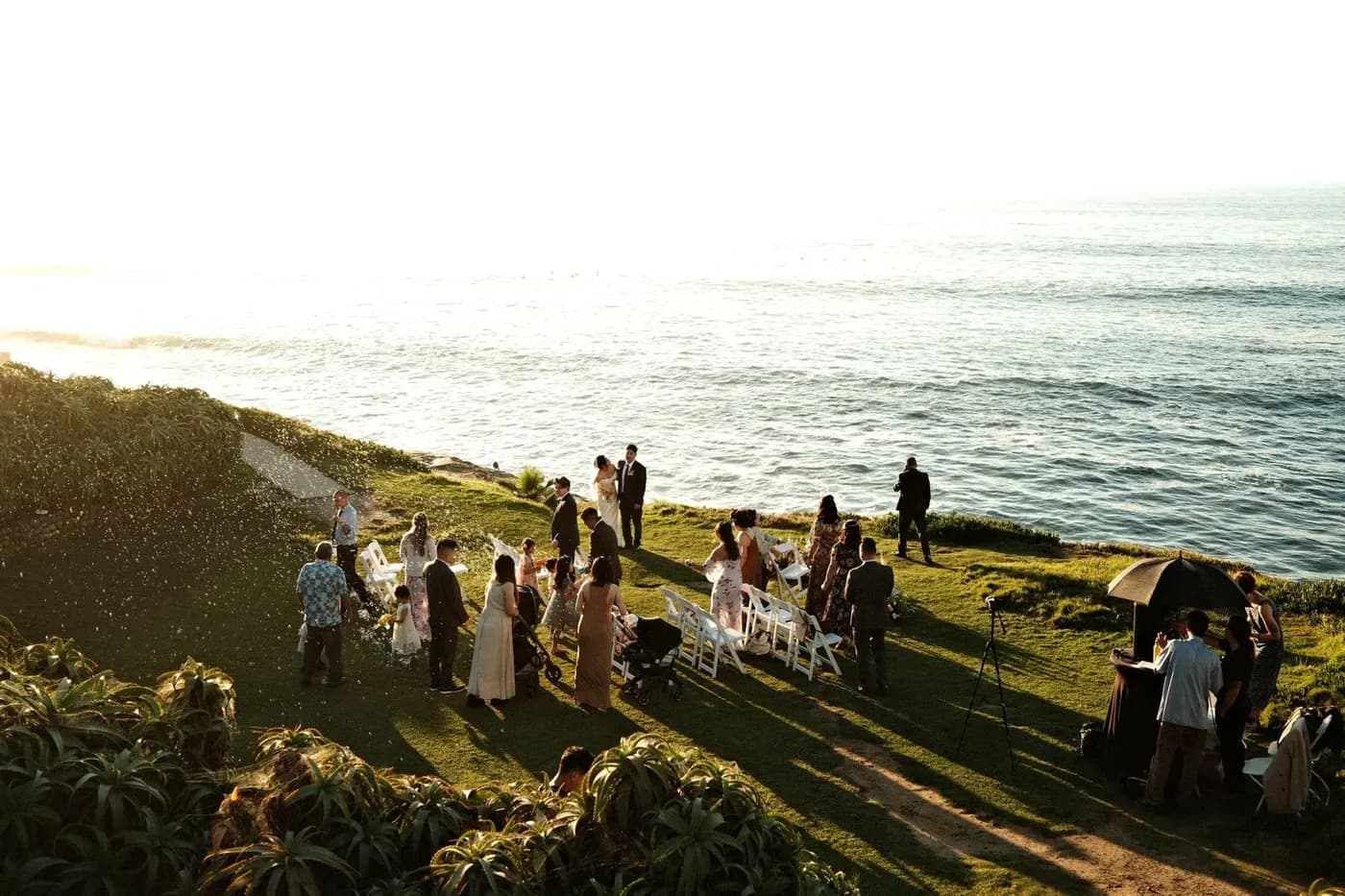 Guests seated on a cliffside deck for a seaside wedding ceremony at sunset