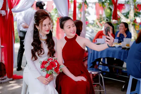 A guest in a red dress taking a selfie with the bride.