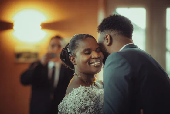 A bride smiling as she slow dances with her groom in warm light.