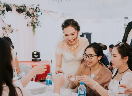 A bride laughing with friends around a reception table.