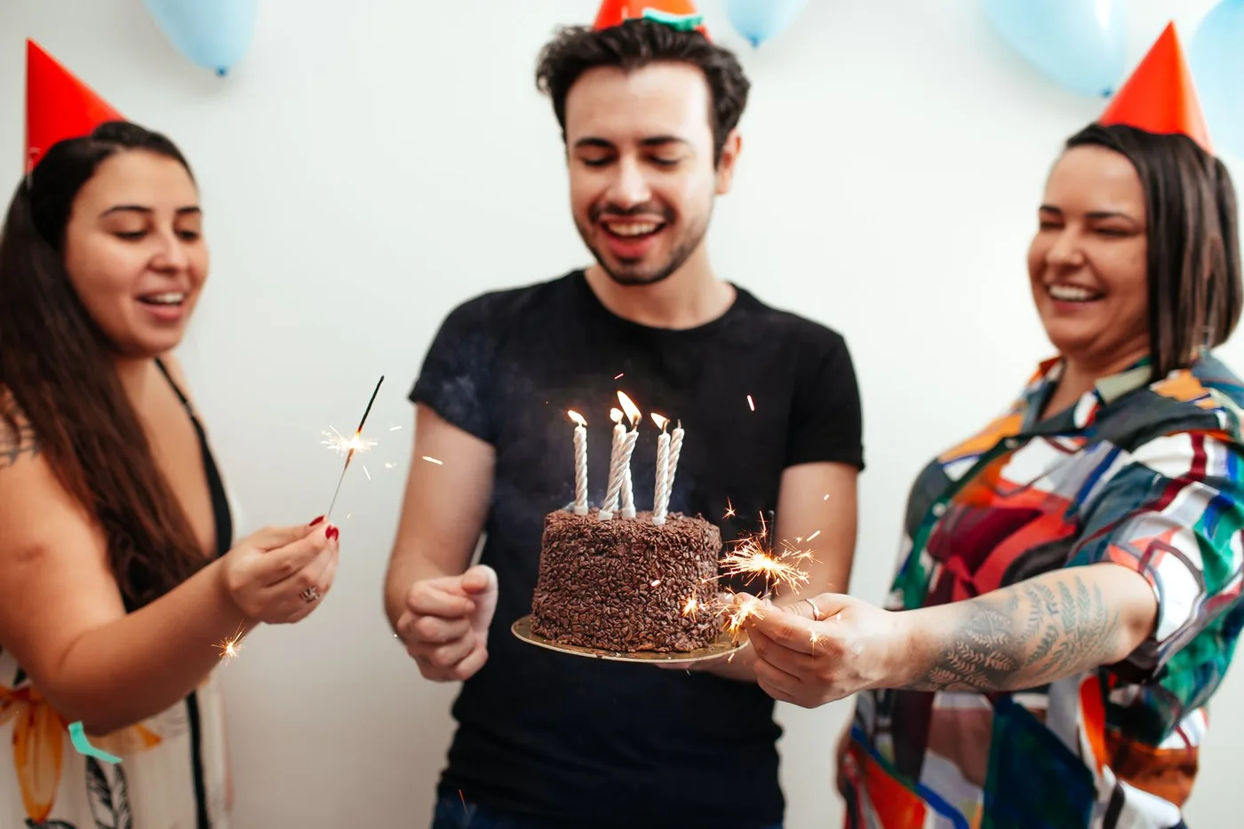 Three friends laughing around a birthday cake with candles and sparklers