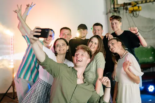 A group laughing and gathering around a phone for a selfie